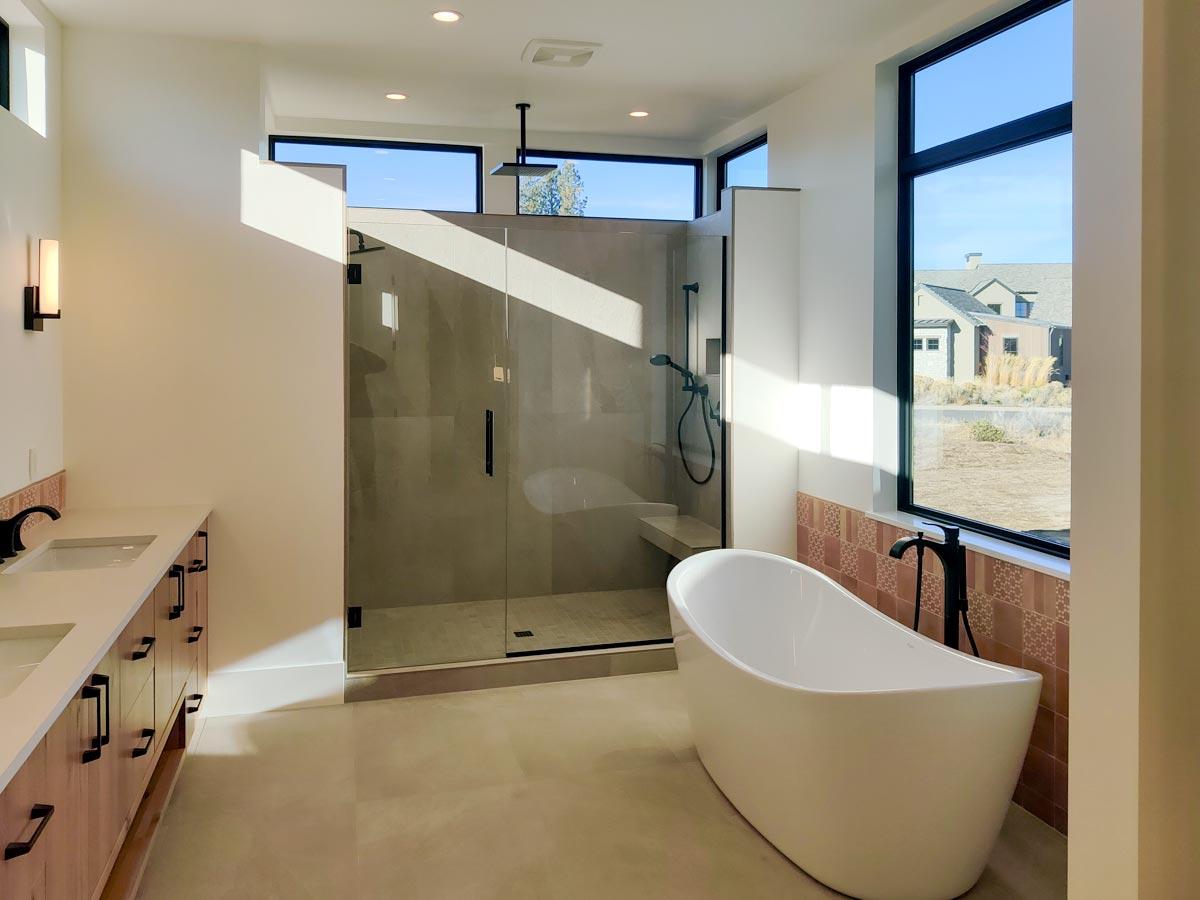A modern bathroom showcases a freestanding tub and a glass-enclosed shower, bathed in sunlight from large windows overlooking the outdoors.