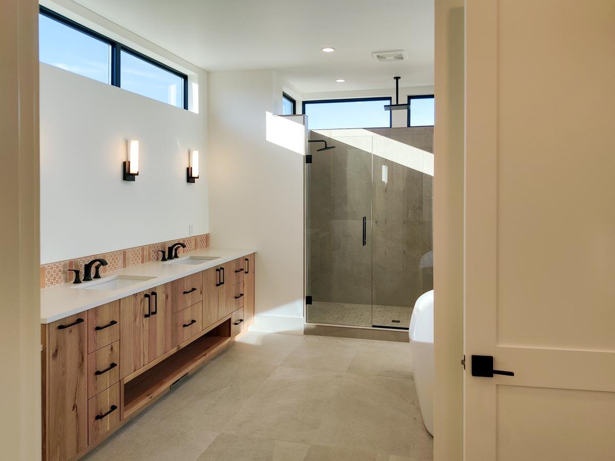 Modern bathroom with a double vanity featuring wood cabinets. A glass shower and a partially visible white bathtub are in the background.