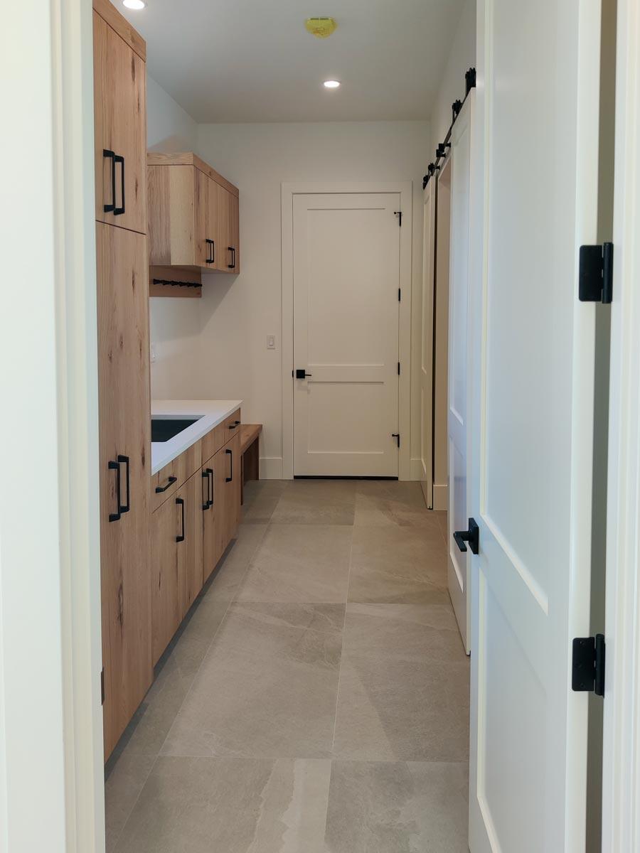 A hallway with light wood cabinetry and a white countertop. A white door is at the end, and another on the right with a black sliding door hardware.