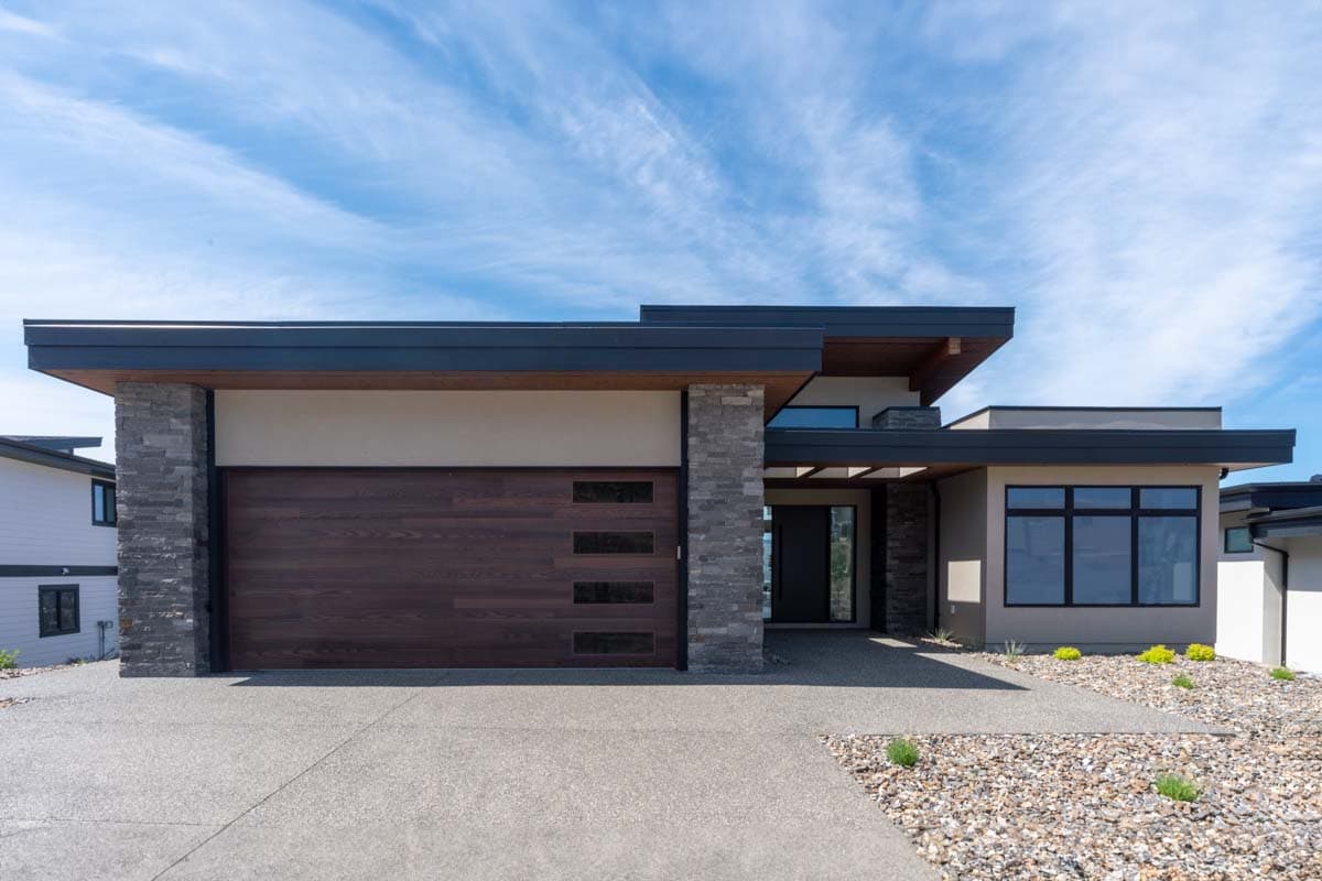 Modern house plan exterior with flat rooflines, stone accents, wood garage door, and prominent entry.