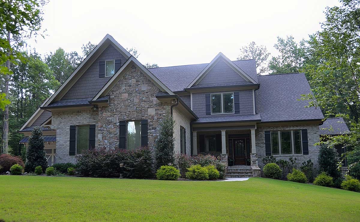 House plan exterior: Two-story home with stone and brick facade, prominent gables, and covered front porch.