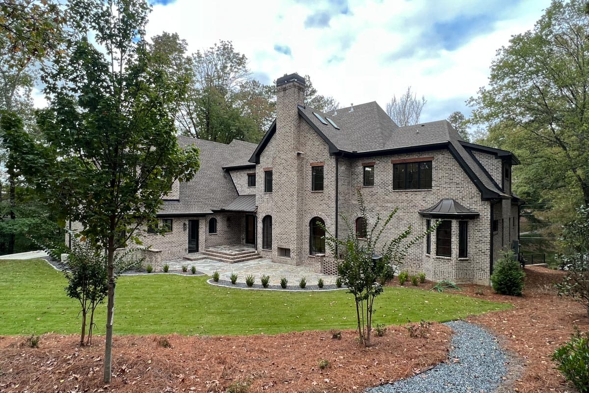 House plan exterior: Brick two-story home with steep rooflines, prominent chimney, bay window, and covered porch.