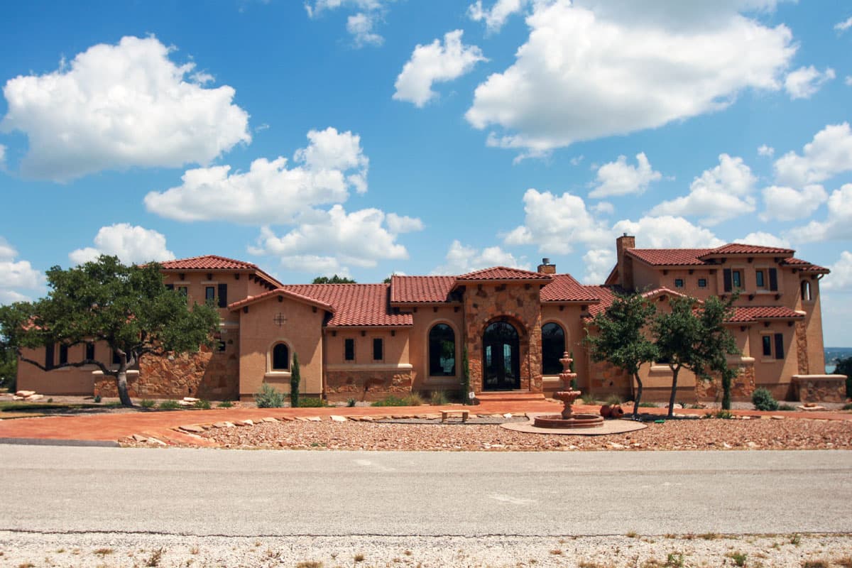 House plan exterior. Two-story Mediterranean-style home with arched entry, red tile roof, and stone facade accents.