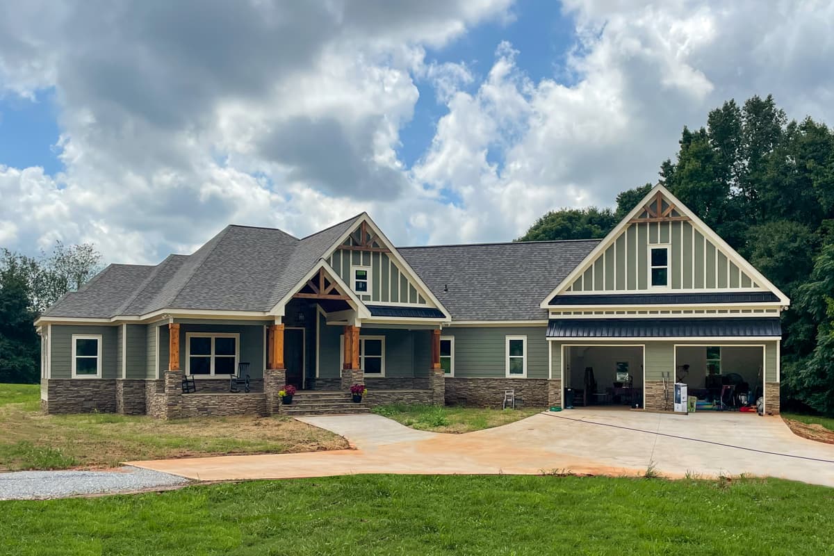 House plan exterior: Ranch style with stone base, large front porch with timber supports, and a three-car garage.
