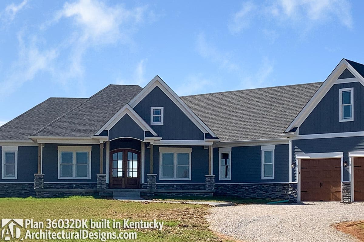 House plan exterior: Single-story home with prominent gables, stone accents, covered entry with double doors, and attached garage.