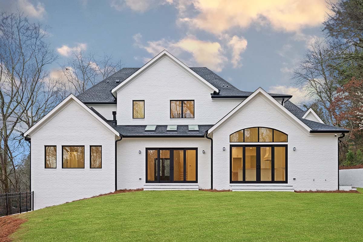 Modern house exterior with white brick, multiple gables, skylights, and a large arched window.
