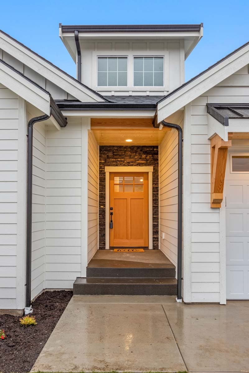 Modern Farmhouse house plan exterior with a covered entryway, wood-trimmed ceiling, stone accent wall, and two upper windows.
