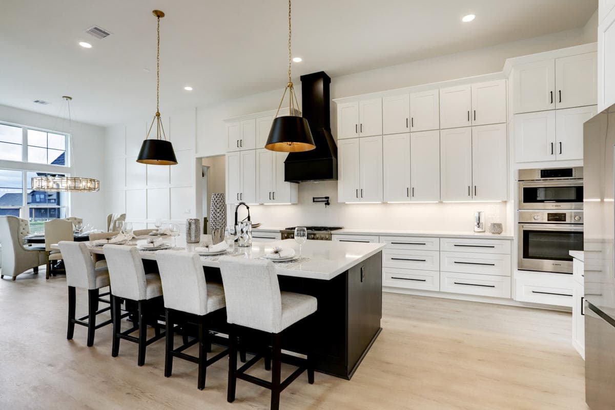 Modern, bright kitchen with a large island and seating. White cabinets, black accents, and pendant lighting create a sleek, contemporary space.