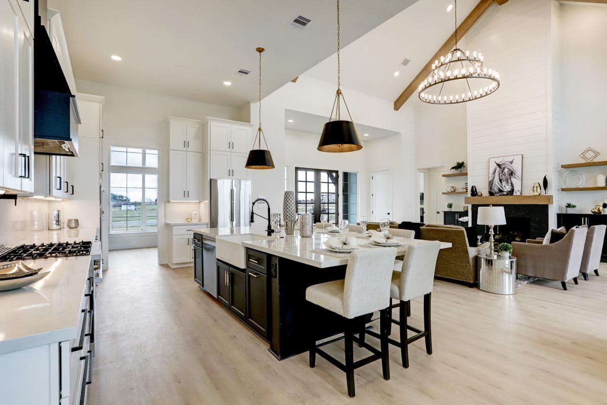 Spacious, modern kitchen with a large island and seating. Features include high ceilings, a fireplace, and elegant pendant lighting.
