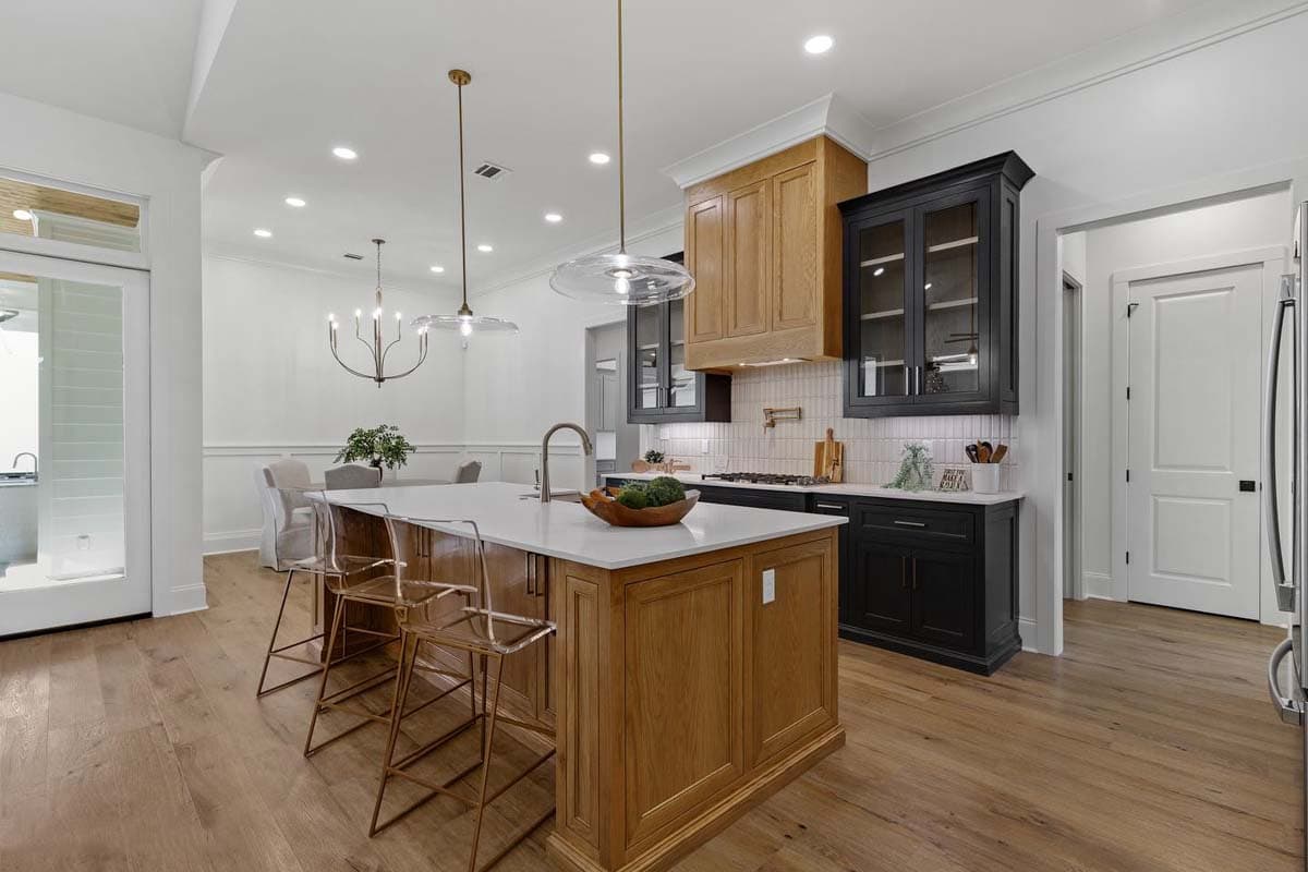 Kitchen with large wooden island, dark cabinetry, light tile backsplash, and pendant lights. Open to dining area.