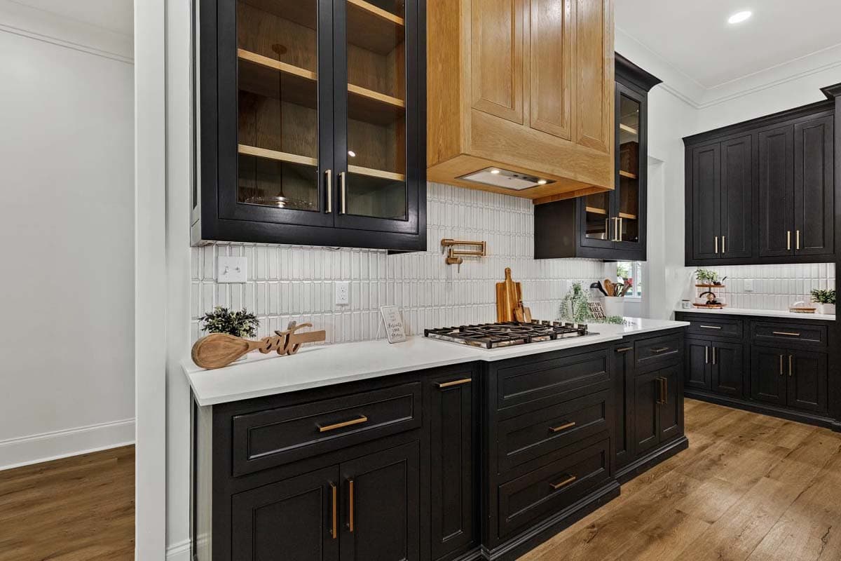 Interior view of a kitchen featuring black cabinetry, a gas range, white tile backsplash, and wood accents on the range hood.