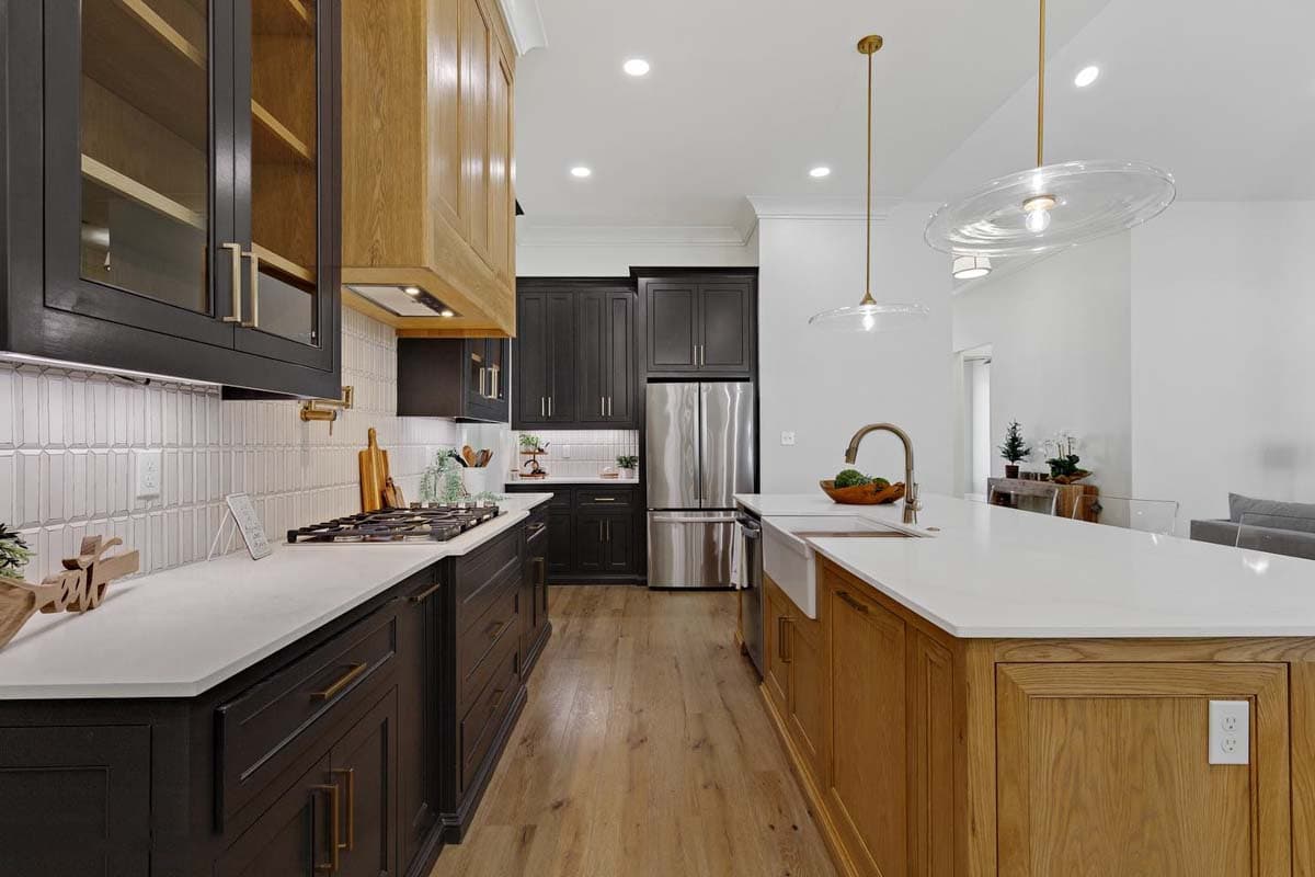 Modern kitchen with dark and natural wood cabinetry, white countertops, gas range, farmhouse sink, and stainless steel refrigerator.