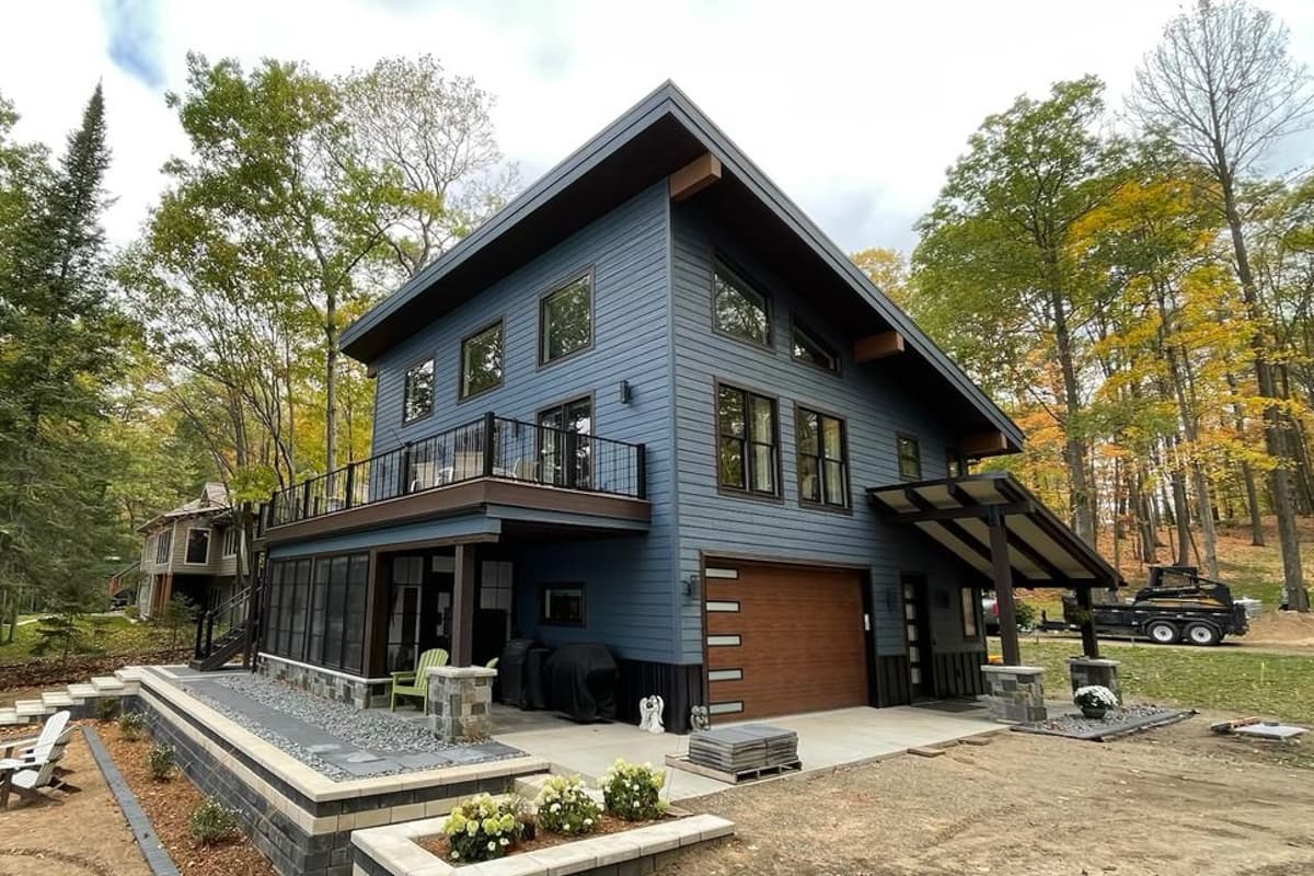 House plan exterior with two stories, a shed roof over the entry, a balcony with a black railing, and a modern garage door.