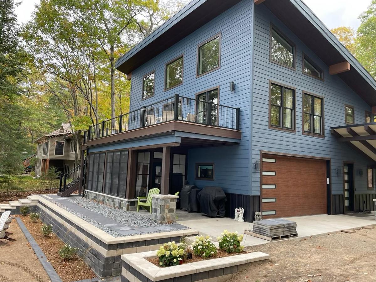 Modern house plan exterior with blue siding, multi-level decks, large windows, and a wood-finish garage door.