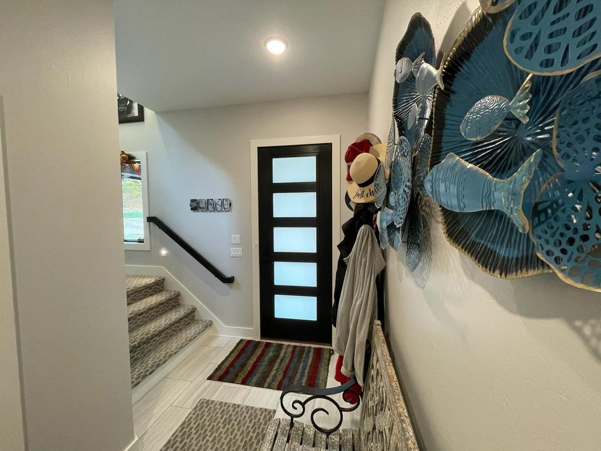 Interior view of a staircase leading past a black door with frosted glass panels and a coat rack with hats.