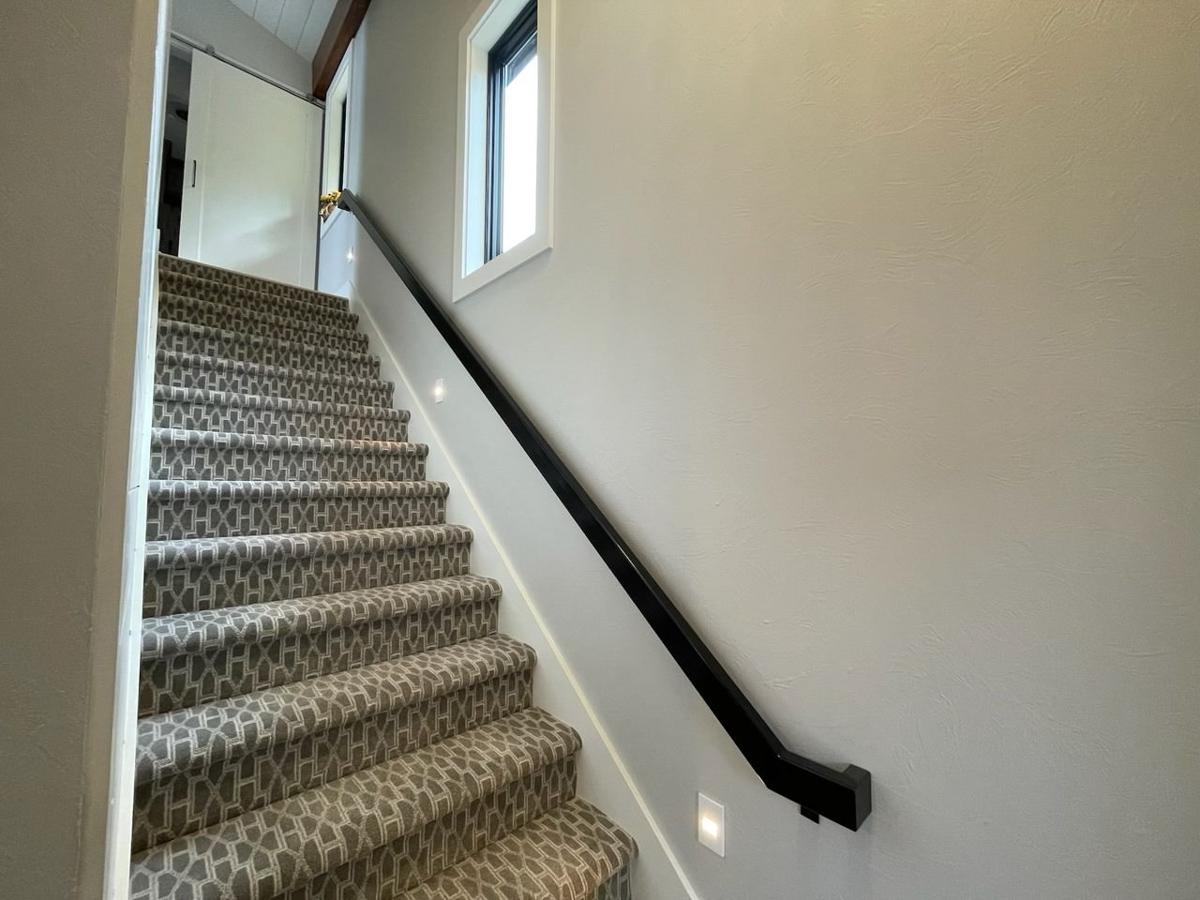 Carpeted staircase with geometric pattern, black handrail, modern window, and recessed stair lights.