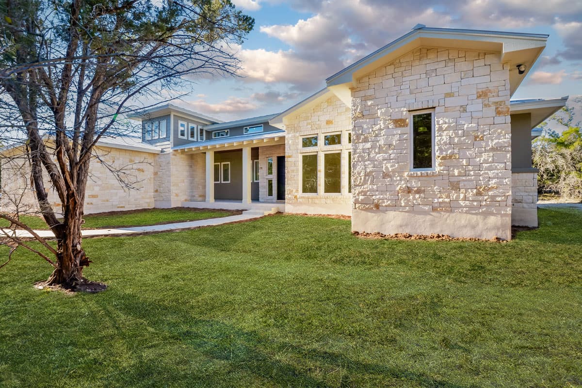House plan exterior. Modern style home with stone veneer facade, gabled roof, and covered porch. Features multiple windows and a flat roof section.