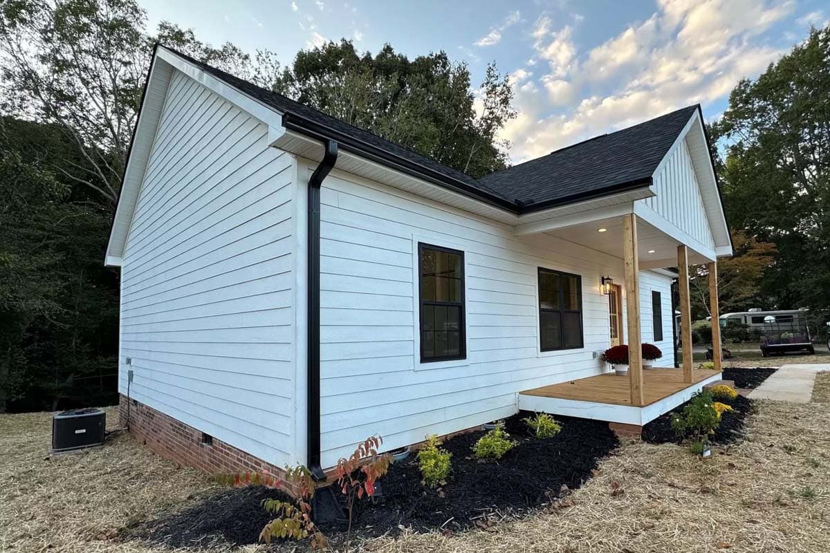 Modern Farmhouse style house plan exterior. One story, white siding, gable roof, and front porch with wooden posts.