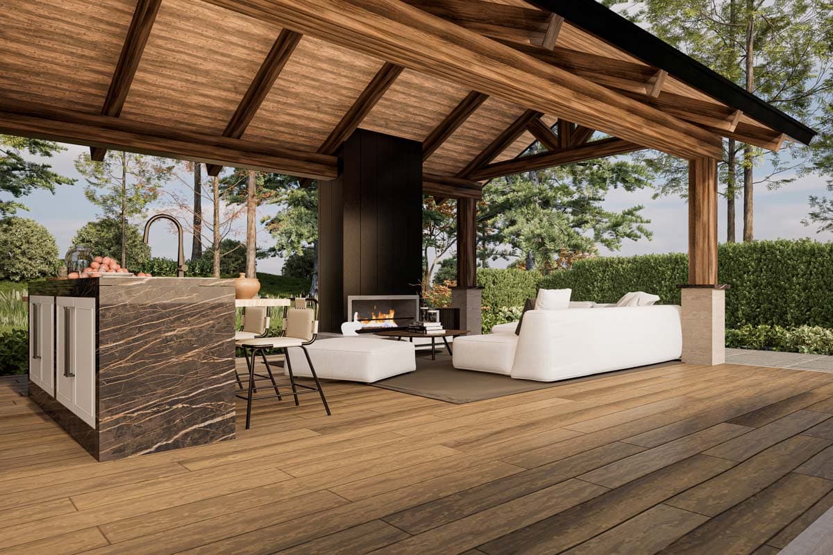 Covered outdoor living space with kitchen island, fireplace, and seating area under a wooden beamed ceiling.