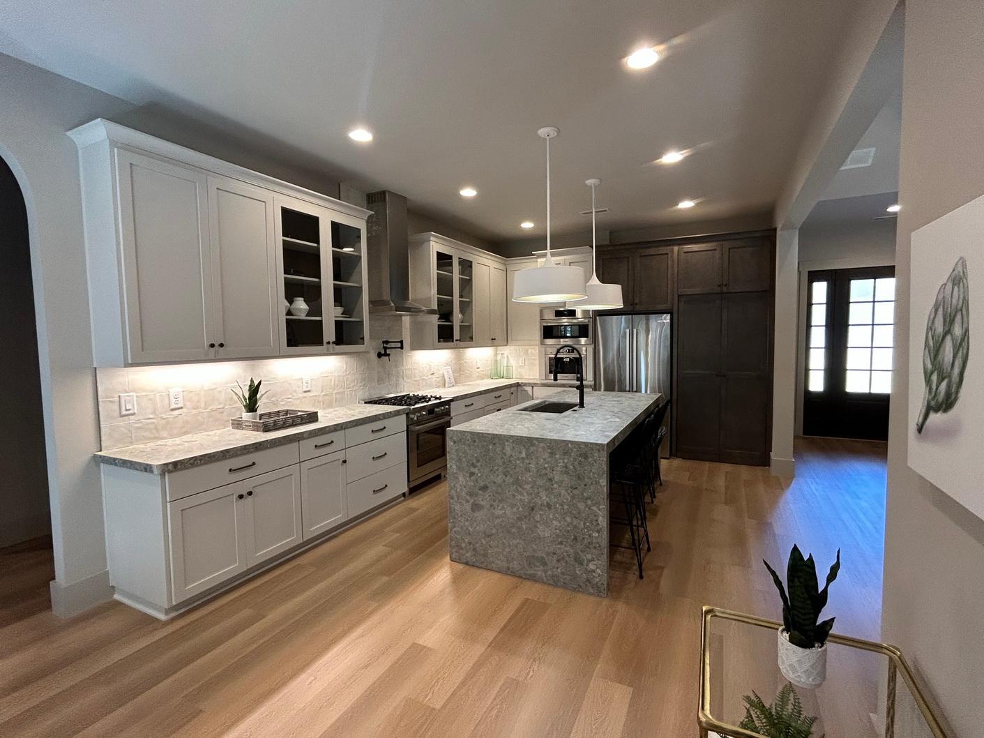 Modern kitchen with a large island, grey quartz countertops, white cabinetry, stainless steel appliances, and a tiled backsplash.