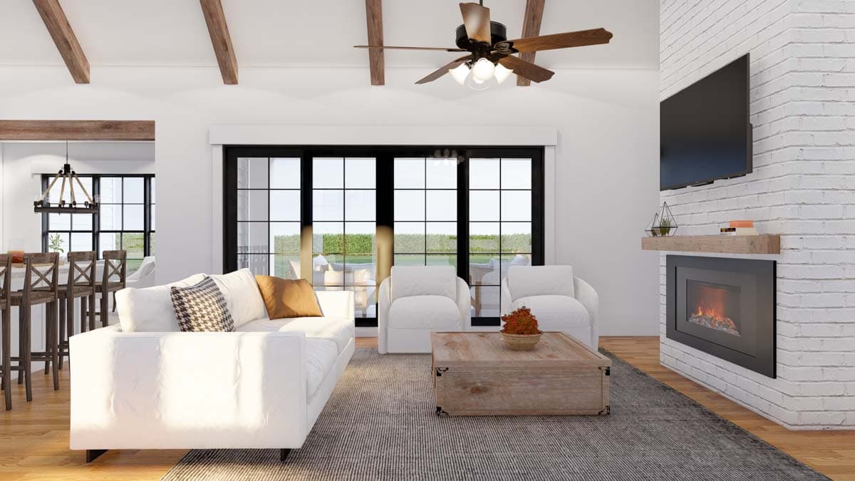 Living room with white sectional, fireplace, exposed beams, large windows, and adjacent dining area with island.