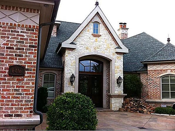 House plan exterior with brick facade, stone entry gable, arched doorway, and pitched roof.