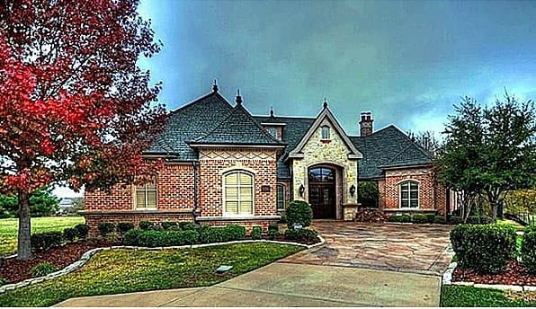 House plan exterior: Two-story brick home with stone accents, arched entryway, multiple gables, and a dormer.