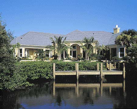 House plan exterior of a one-story home with arched windows, a hipped roof, and a dock on the water.