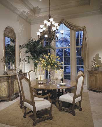 Dining room with round table, upholstered chairs, ornate chandelier, and large bay window with draped curtains.
