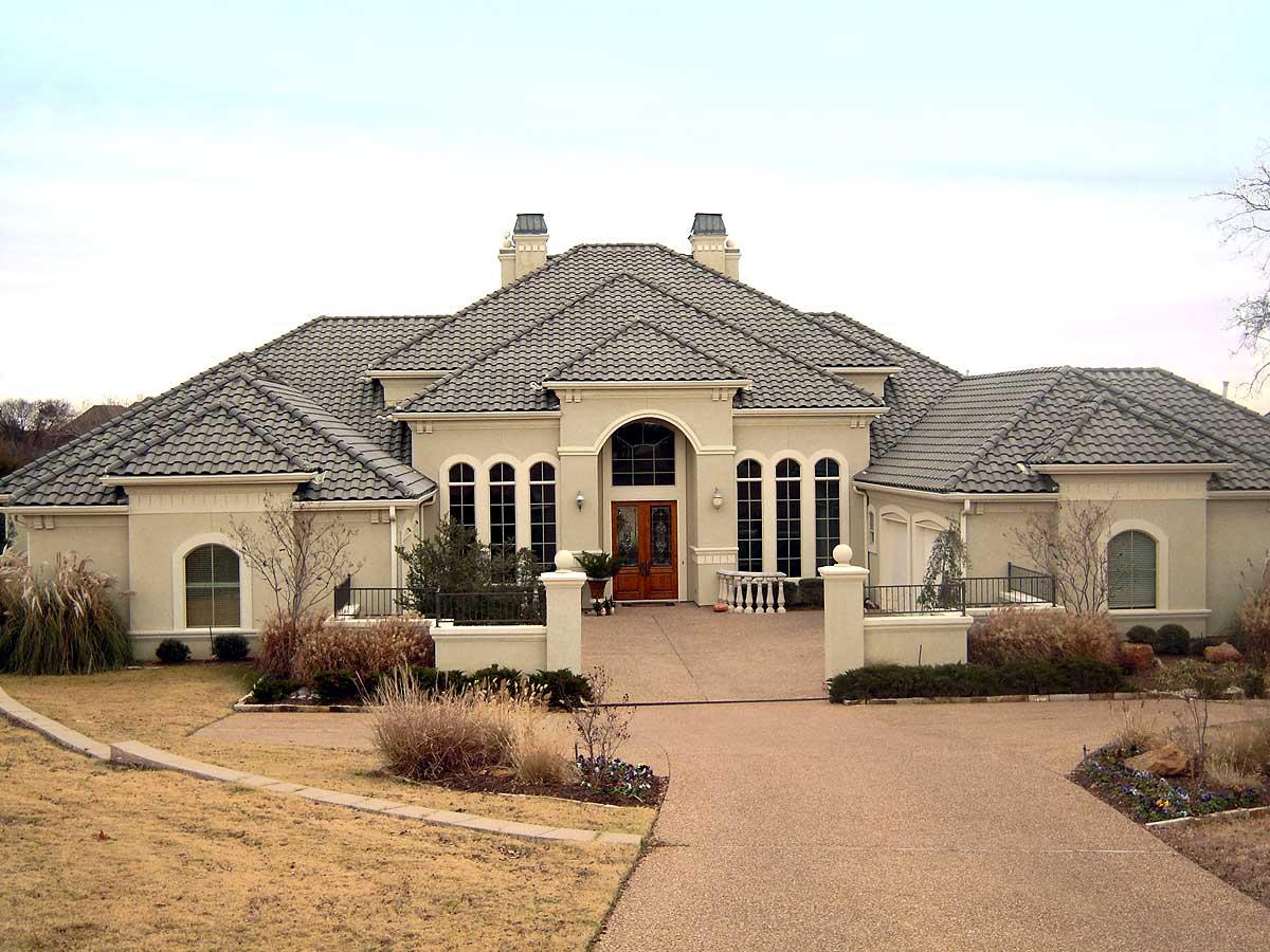 House plan exterior. Two-story Mediterranean-style home with tile roof, arched windows, and a portico over the front entrance.