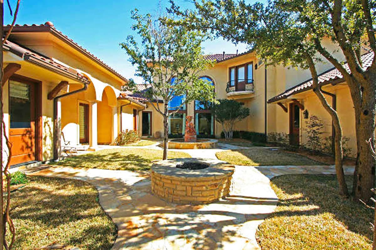 House plan exterior with stucco walls, arched loggias, tile roof, and central courtyard with fire pit.