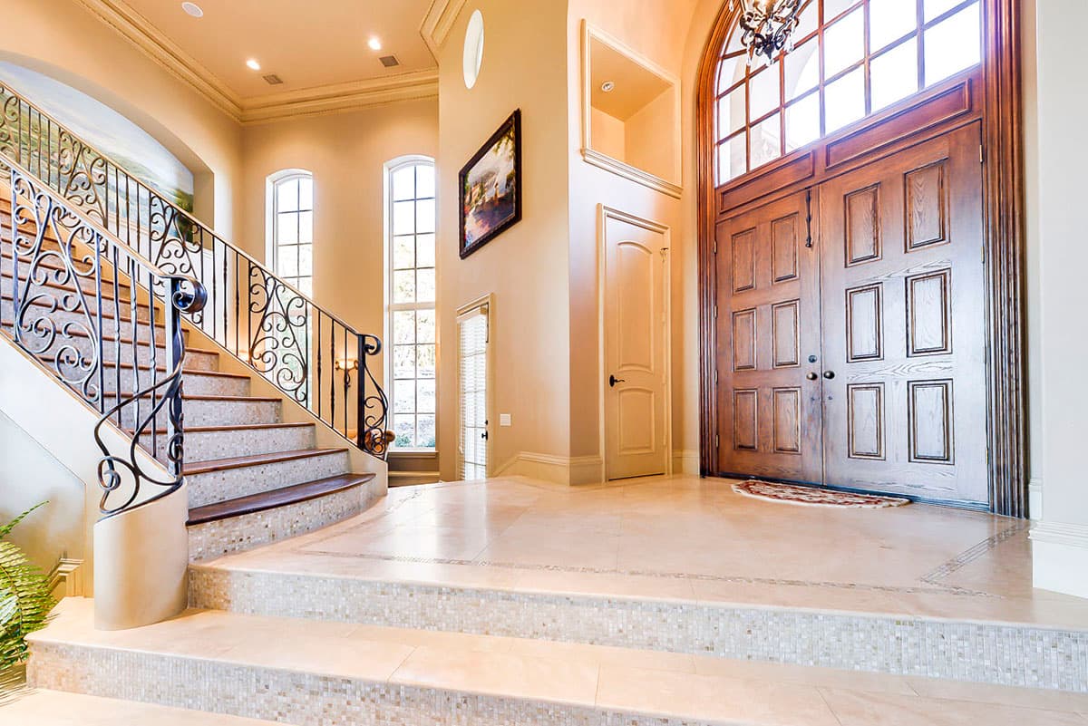 Foyer with curved staircase, double wooden doors, arched transom window, and tall windows.