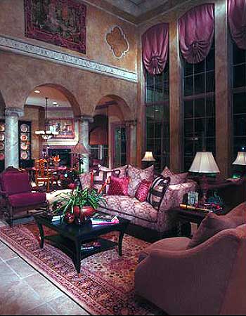 Interior view of a living room with a patterned sofa, dark wood coffee table, fireplace, and arched doorways leading to a dining area.