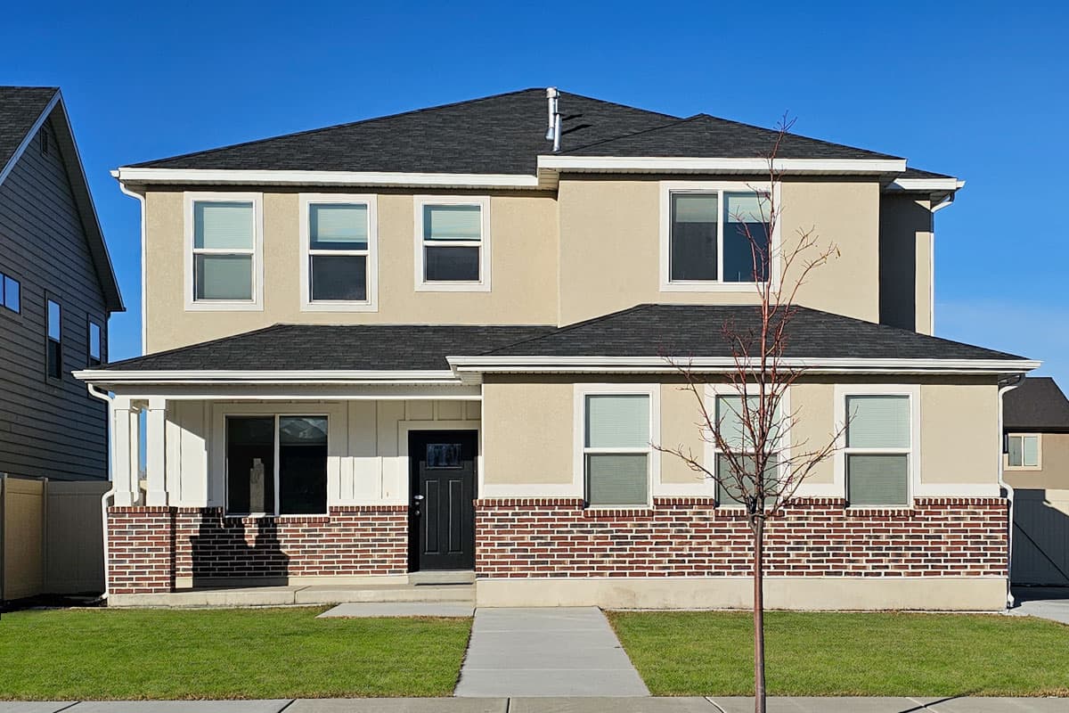 Two-story house plan exterior with a gabled roof, brick facade, and covered front porch with white columns.