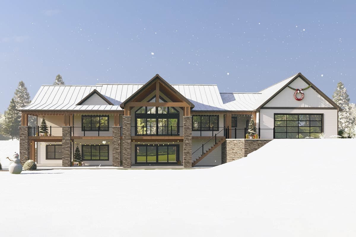 A modern, two-story house with a snowy roof and stone accents, decorated for Christmas with wreaths, trees, and lights.
