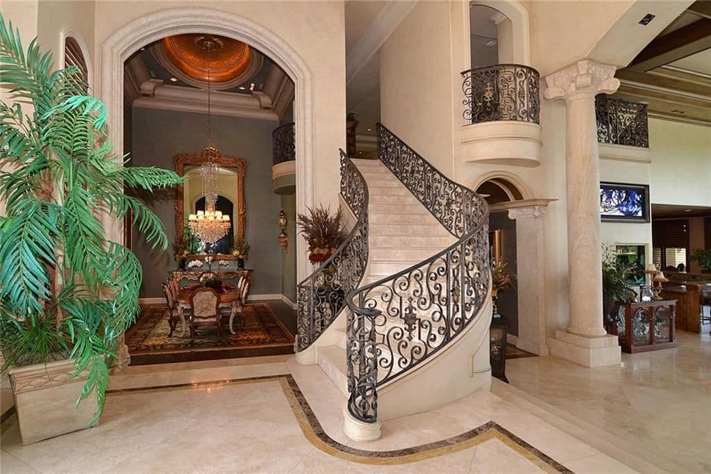Grand foyer with a curved staircase, wrought iron railings, arched entryway to dining room, and a domed ceiling.