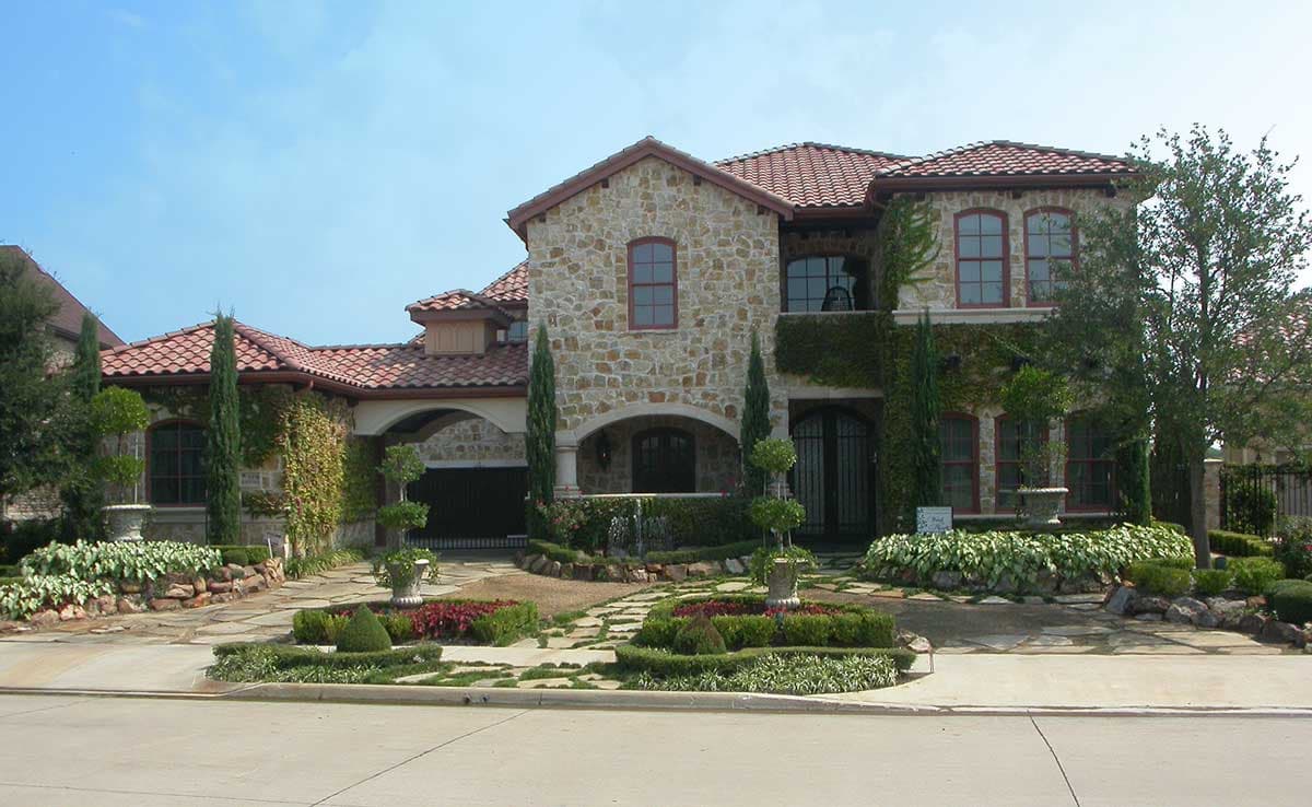 Two-story house plan exterior with stone facade, arched entryway, tile roof, dormers, and ivy accents.