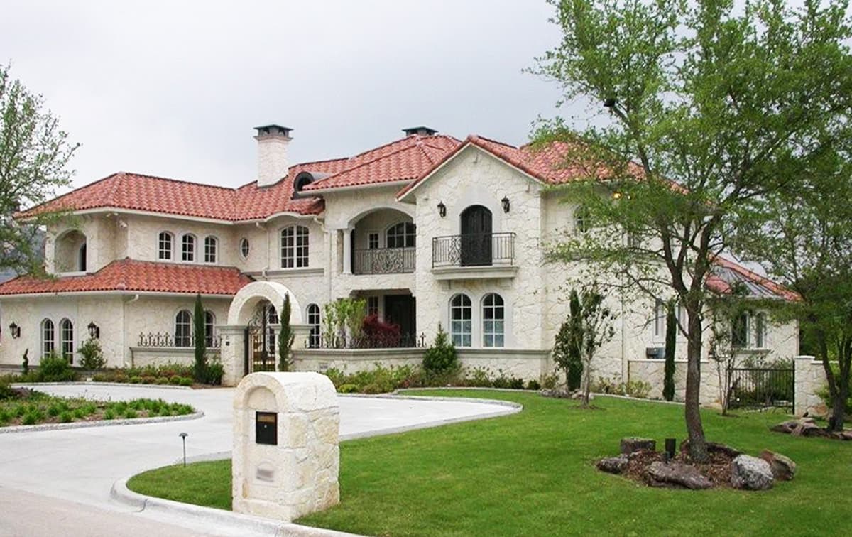Mediterranean-style house plan exterior with red tile roof, stucco finish, arched windows, balconies and a gated entrance.