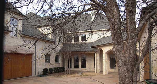 House plan exterior: Stone-clad multi-story home with hip roof, arched entryway, and attached multi-car garage.