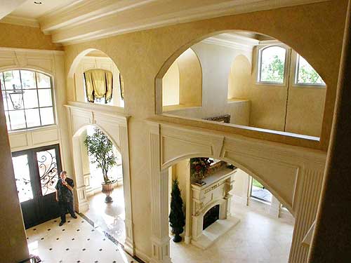 Interior view of a grand foyer with arched doorways, a fireplace, a tall window, and decorative molding.