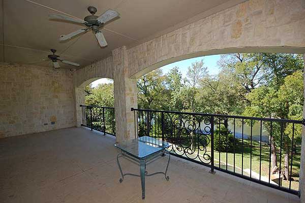 Covered outdoor living area with stone walls, two ceiling fans, decorative metal railing, and a glass-top table.
