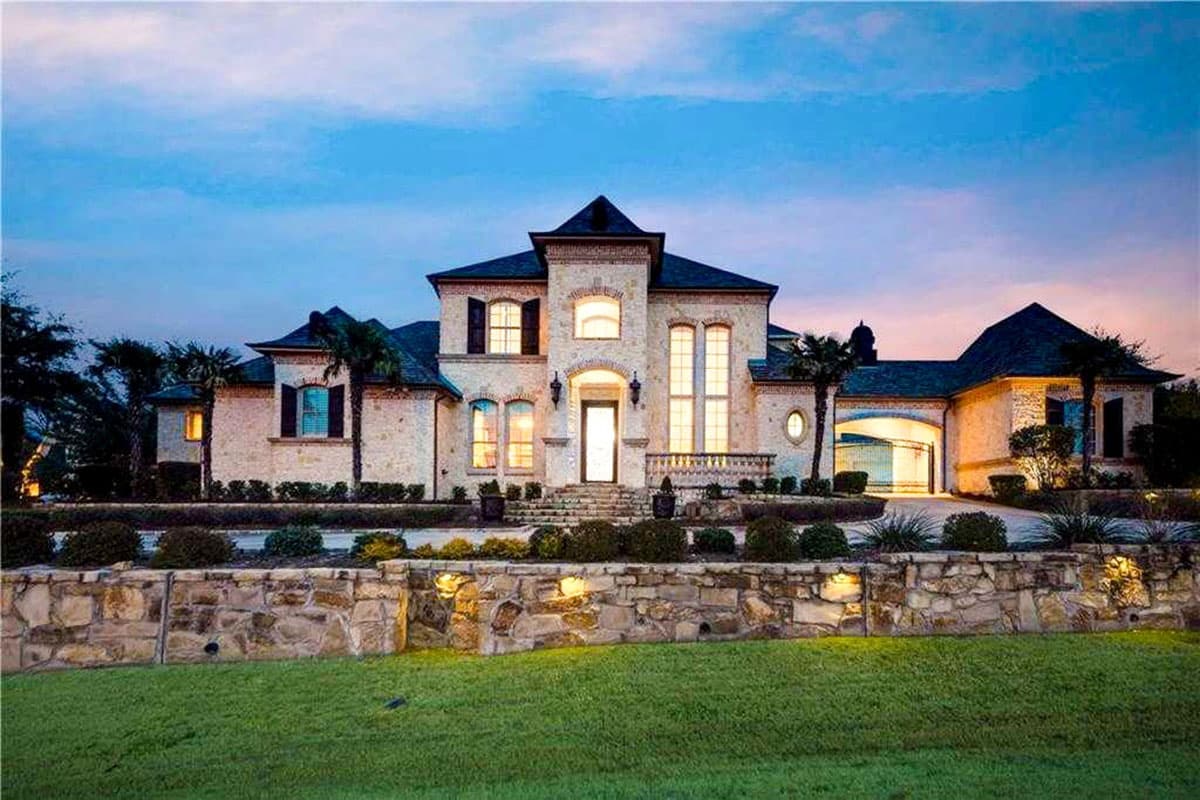 House plan exterior: two-story home with stone facade, arched entryway, multiple gables, and attached garage.
