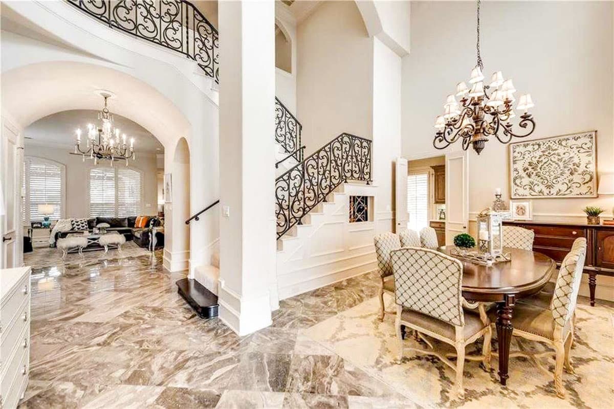 Interior view: Formal dining area with oval table and chairs adjacent to a living room with sectional sofa. Ornate iron railing staircase.