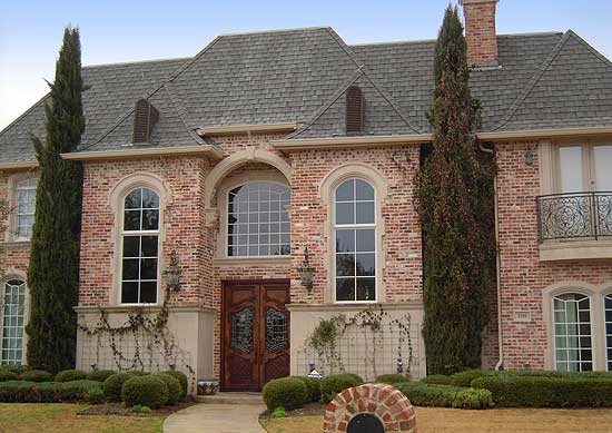 House plan exterior: brick facade, multiple arched windows, prominent double doors, and a slate roof.
