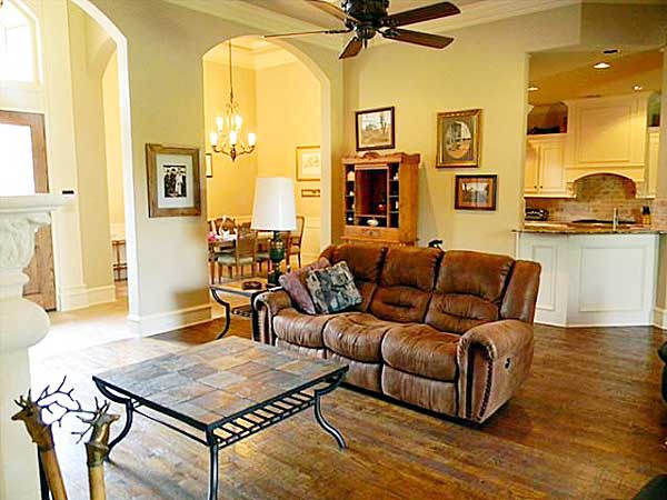 Interior view of a living room with a leather sofa, coffee table, and arched doorways leading to a dining area and kitchen.