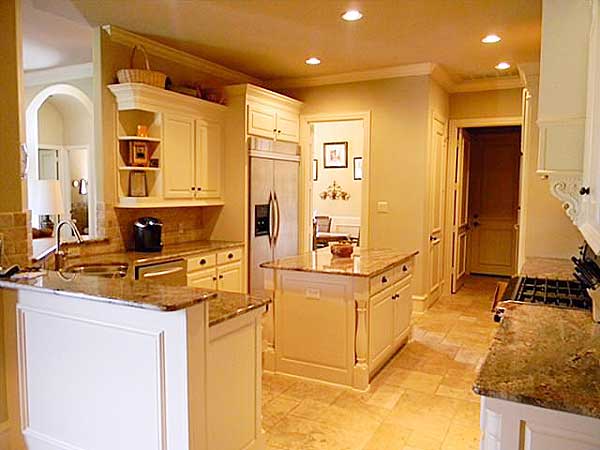 Kitchen with granite countertops, central island, white cabinetry, stainless steel refrigerator and gas range.
