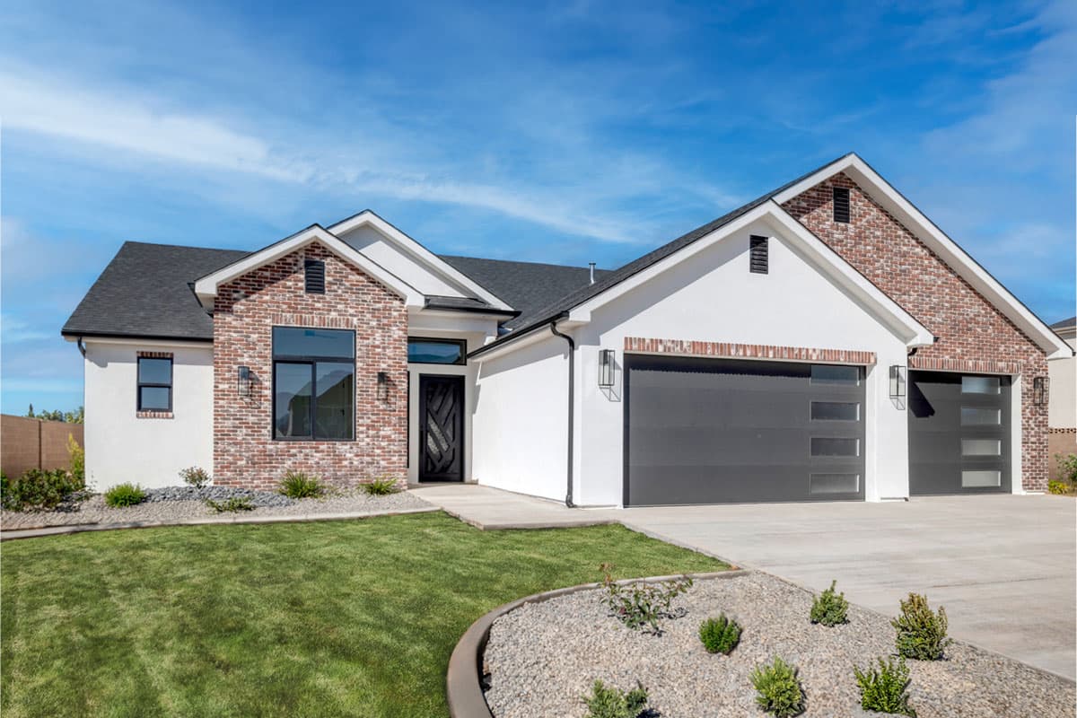House plan exterior. One-story modern house with brick and stucco facade, featuring a side-entry garage, gable roof, and large windows.