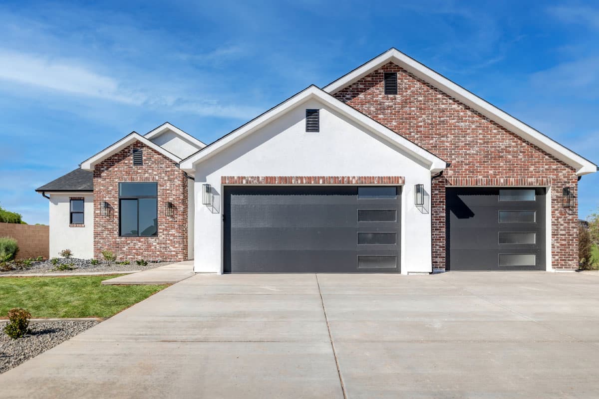 House plan exterior with white stucco, red brick accents, and two modern garage doors with glass panels.