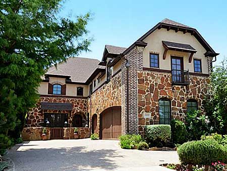 House plan exterior with stone and brick facade, multiple gables, arched garage, and second-story balcony.