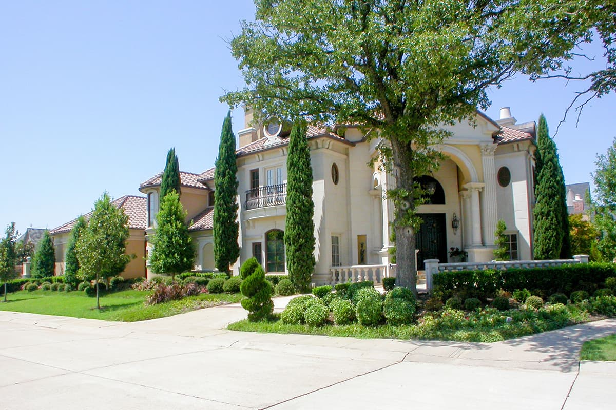 House plan exterior view of a multi-story estate with a tile roof, arched entryway, balustrade, and manicured landscaping.